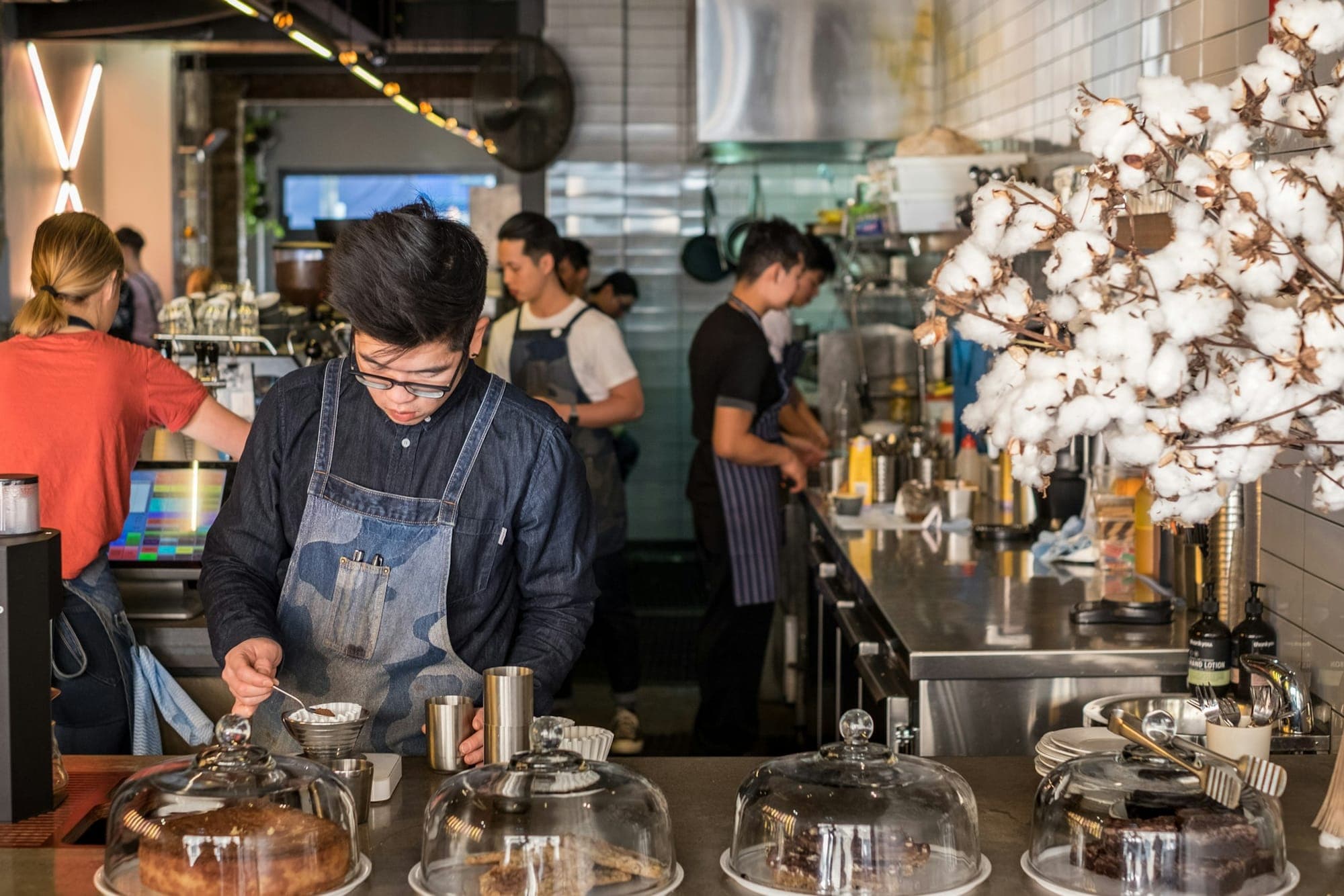 A café team at work behind a counter of cakes under glass domes