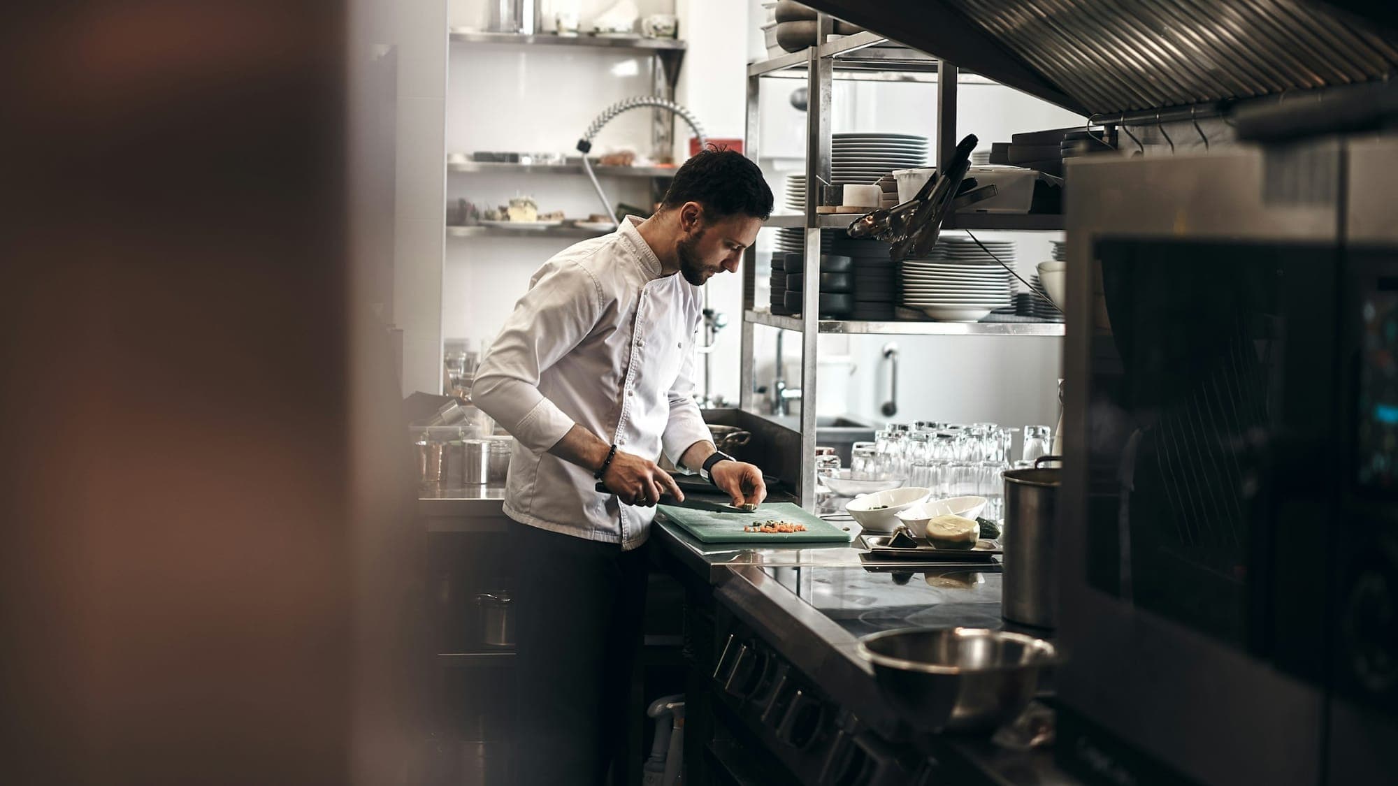 A chef working at a stainless counter in a dim kitchen at the end of service